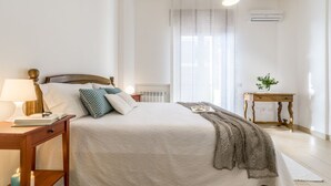 Une chambre bien rangée, avec un lit, une table de chevet, une lampe et une petite table sur laquelle est posée une plante.