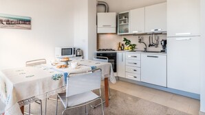 Une cuisine moderne avec des meubles blancs, une table à manger recouverte d’une nappe en dentelle et un tableau accroché au mur.