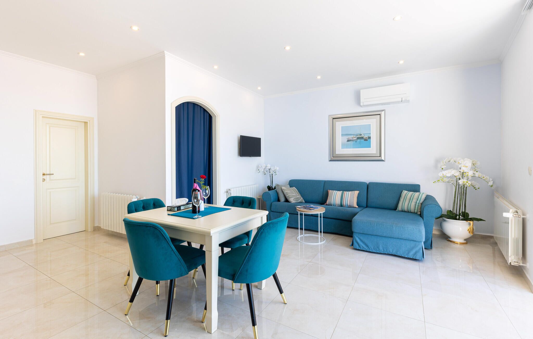 Een moderne woonkamer met een blauwe bank, blauwgroene stoelen en een eettafel.