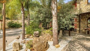 A courtyard with palm trees, a stone wall, and a rustic building. - 3 bedroom pet friendly home in Imperia (Imperia)