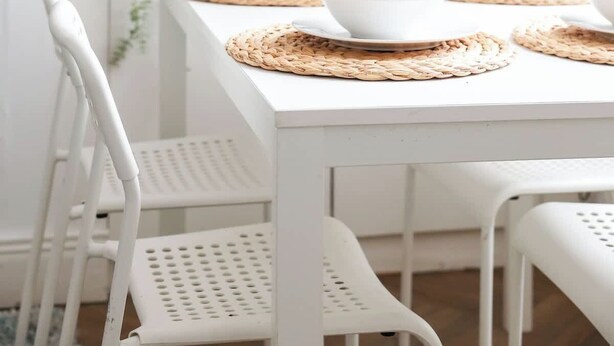 Une table à manger blanche, avec des sets de table, des chaises blanches et des plantes vertes en arrière-plan.
