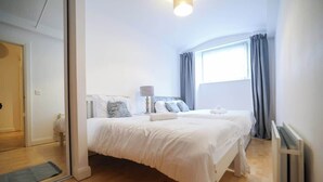 Et soveværelse med seng, sengebord, lampe og et vindue med gardiner.