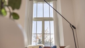Et værelse med et stort vindue, en sofa med puder og en gulvlampe.