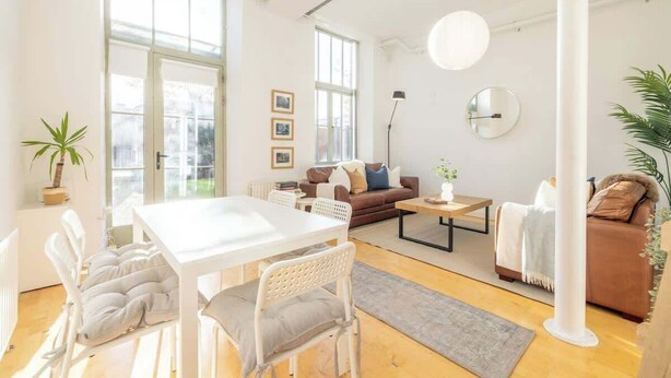 En lys stue med et hvidt bord, stole, en brun sofa og et sofabord.