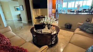Uma sala de estar espaçosa com um sofá bege, uma mesa de centro com um vaso de flores e uma grande janela com vista para a cidade.