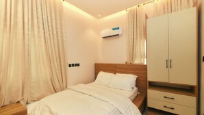 A bedroom with a bed, a wardrobe, and an air conditioning unit. - AJs Serenity Suites (Abuja)