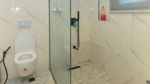 A modern bathroom with a glass-enclosed shower, a toilet, and a small shelf with toiletries. - AJs Serenity Suites (Abuja)