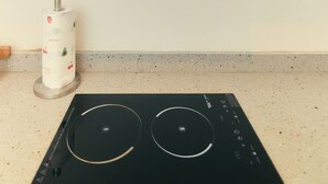 A kitchen with a POLYSTAR range hood, a white paper towel dispenser, and a black induction cooktop. - AJs Serenity Suites (Abuja)