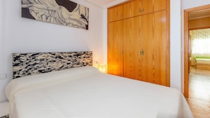 Une chambre à coucher avec un lit, une armoire en bois, un tableau au mur et une lampe.