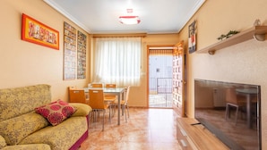 Un salon avec un canapé, une table à manger et des chaises, un téléviseur et une porte-fenêtre donnant sur un balcon.