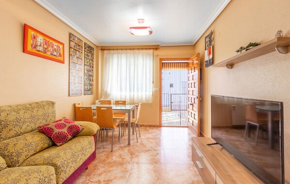 Een woonkamer met een bank, een eettafel met stoelen, een televisie en een openslaande deur naar een balkon.