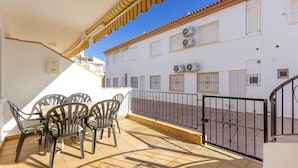 Un balcon avec une table et des chaises, un sol carrelé et un bâtiment blanc avec des fenêtres et des unités de climatisation en arrière-plan.