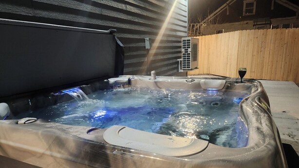 Ein Whirlpool mit einer Holzdielen-Terrasse und einem Haus im Hintergrund.