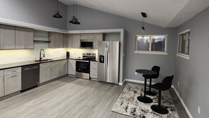 Eine moderne Küche mit grauen Schränken, einem Edelstahl-Kühlschrank und einem Essbereich mit schwarzem Tisch und Stühlen.