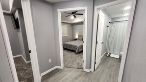 Ein Flur, der zu einem Schlafzimmer mit Bett, Deckenventilator und einem Badezimmer mit Duschvorhang führt.