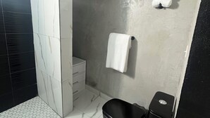 A modern bathroom with a walk-in shower, a black bathtub, and a white towel hanging on the wall. - Molinos House 1 (Santa Isabel)