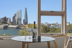 A table with two glasses and a bottle, a window with a cityscape view, and a chair. - Magical Sydney Escape with Harbour Views & Parking (McMahons Point)