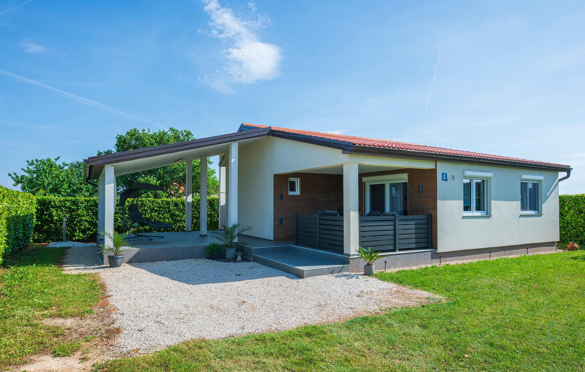 A modern single-story house with a covered patio, a gravel driveway, and a well-maintained lawn.
