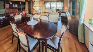 Ein Esszimmer mit einem runden Tisch, Stühlen, einer Chandelüster und Blick ins Freie durch große Fenster.