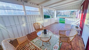 Eine überdachte Terrasse mit Korbmöbeln, einem Glastisch und Blick auf den Garten.