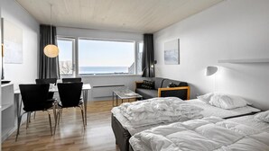 Une chambre d’hôtel moderne dotée d’un grand lit, d’un bureau avec des chaises, d’une vue sur la mer et d’un coin repas.