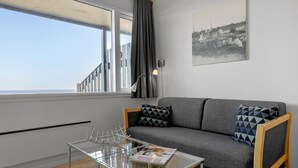 Un salon moderne avec un canapé gris, des coussins à motifs, une table basse en verre et une photographie en noir et blanc encadrée accrochée au mur.