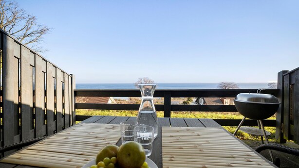 Une terrasse en bois avec une table dressée pour un repas, une vue dégagée sur l’océan et un barbecue.