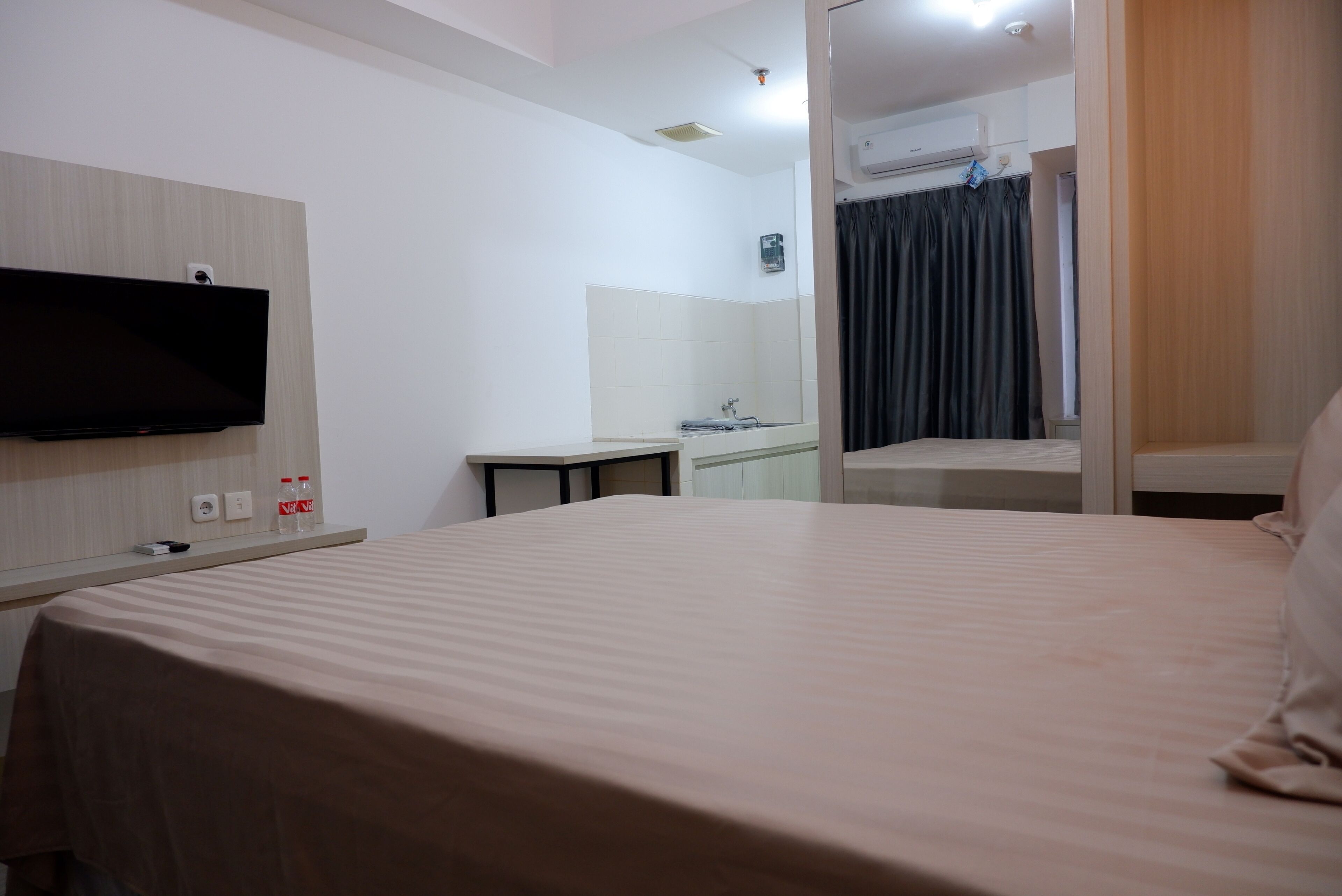Ein Hotelzimmer mit Bett, einem flachbildfernseher an der Wand, einem kleinen Tisch und einem durch eine offene Tür einsehbaren Badezimmer.