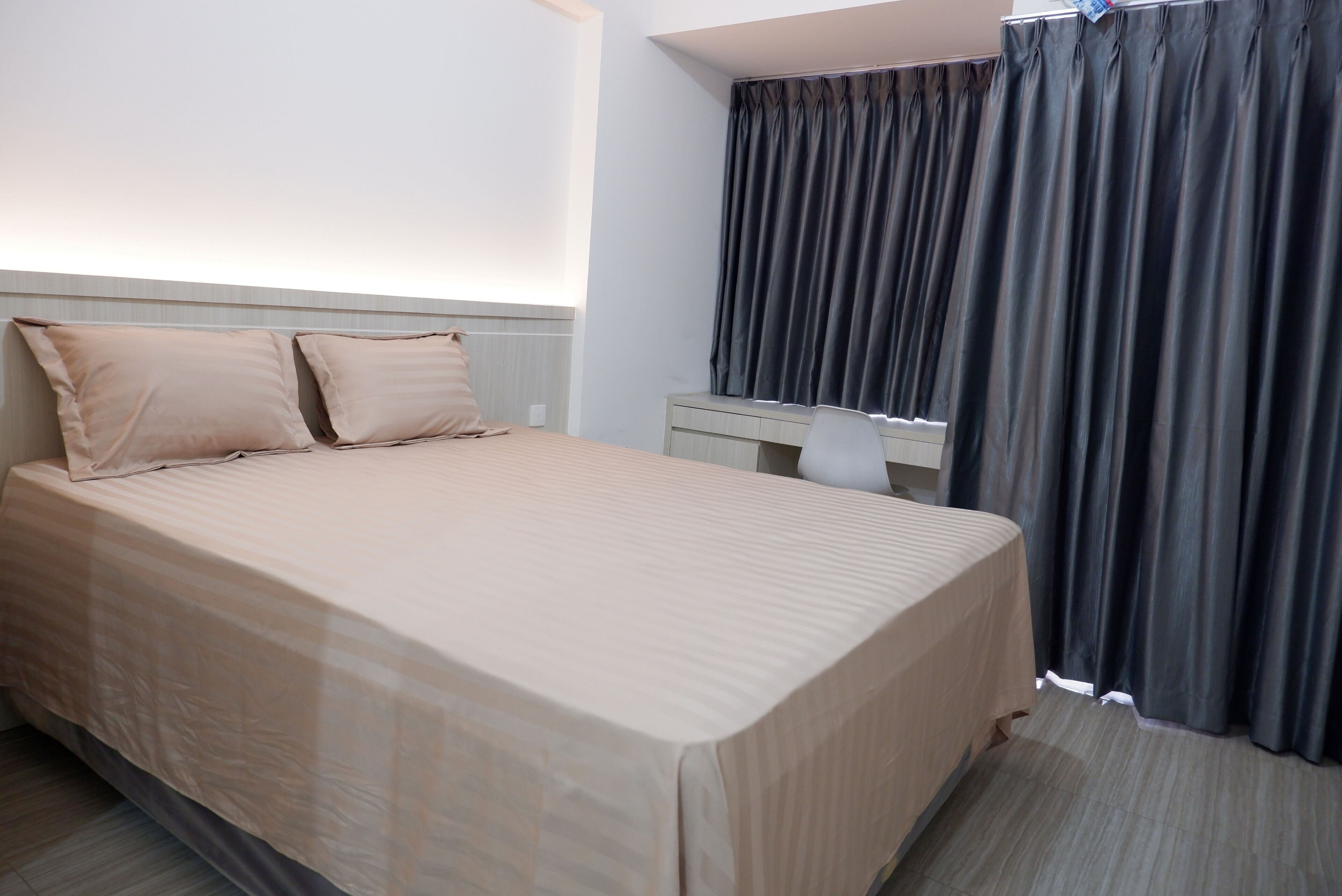 A hotel room with a bed, two pillows, a desk, and a chair.