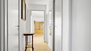 Un pasillo con una mesa de madera, paredes blancas y un aparador de madera al fondo.