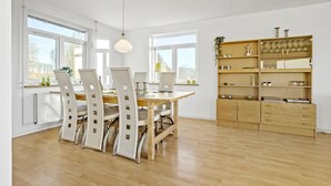 Un comedor espacioso con una mesa y sillas de madera, ventanas amplias y una estantería empotrada.