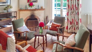 A cozy living room with a fireplace, comfortable seating, and a view of greenery outside.