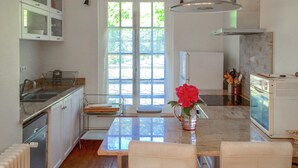 A kitchen with a large window, a dining table, and a vase with flowers.