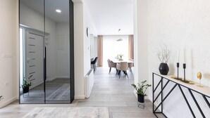 Un couloir moderne et bien éclairé mène à un espace repas comprenant une table et des chaises, une plante en pot et une console décorative agrémentée de bougies.