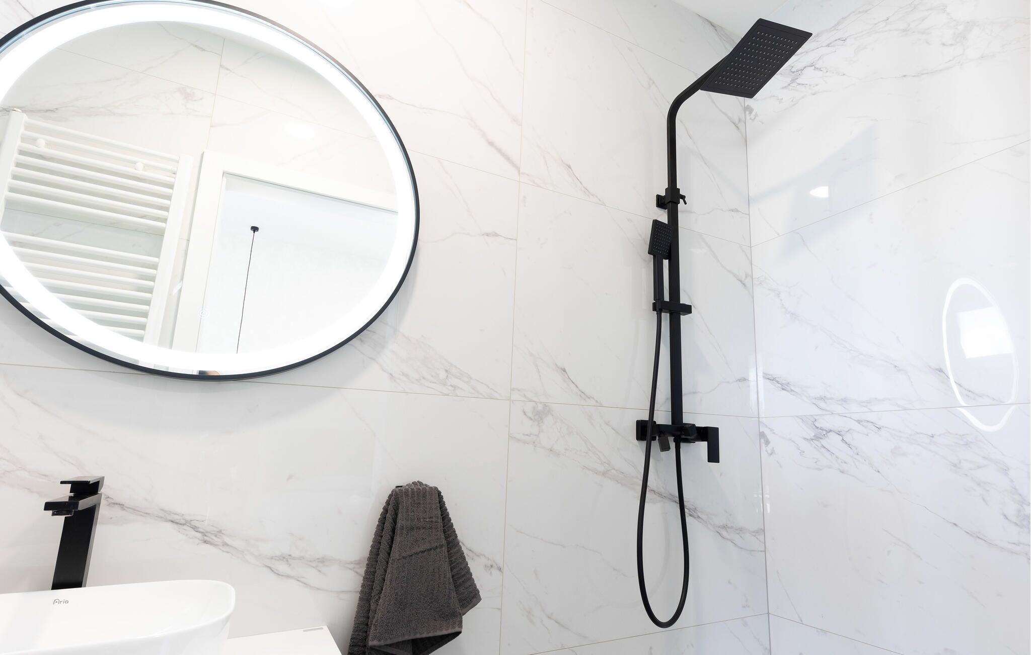 Une salle de bain moderne avec un miroir rond, une douchette à main et un porte-serviettes.