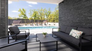 Un espace de vie extérieur moderne, doté d’une piscine, de chaises longues et d’un canapé agrémenté d’un coussin sur lequel est brodé le mot « Bienvenue ».