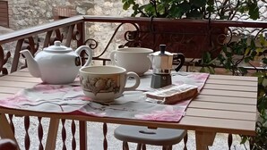 A balcony with a table set for tea, a chair, and a potted plant with red flowers.