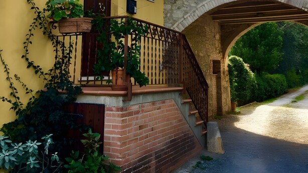 A yellow building with a stone bridge, a wooden staircase, and potted plants.
