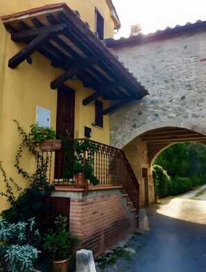 Un bâtiment jaune avec un pont en pierre, un escalier en bois et des plantes en pot.