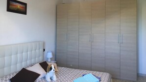 A bedroom with a bed, a wardrobe, a nightstand, a lamp, and a framed picture on the wall.