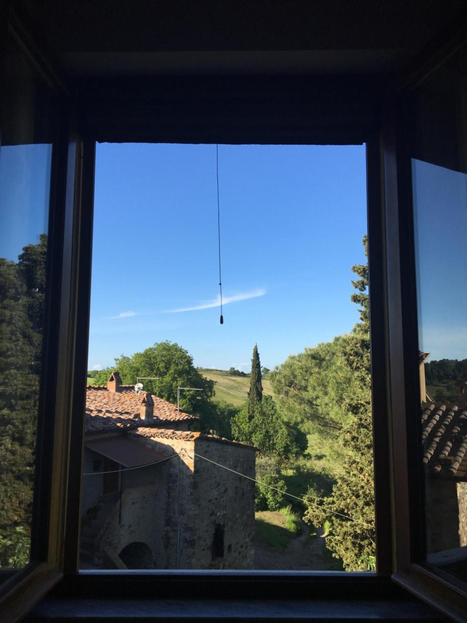 Une vue à travers une fenêtre sur un paysage rural, avec un bâtiment en pierre et des arbres.