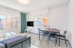 A furnished living room with a sofa, a dining table with chairs, a flat-screen TV mounted on the wall, and large windows with curtains. - Apartment 'Staffan En Santa Pola' with Sea View, Wi-Fi and Air Conditioning (Santa Pola)