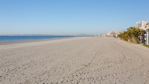 Ein weiter Sandstrand mit blauem Himmel, ruhiger See und Gebäuden entlang der Küste.
