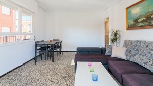 Ein Zimmer mit Esstisch, Stühlen, einer Couch, einem Couchtisch mit Gläsern, einem Gemälde und einem Fenster mit Blick auf Gebäude.