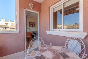 A balcony with a stone table and metal chairs, a white door, and a window overlooking buildings. - Apartment 'Apartamento Salamanca 4' with Shared Pool, Wi-Fi and Air Conditioning (Santa Pola)