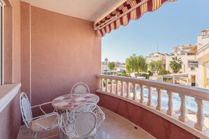 Ein Balkon mit Tisch und Stühlen, Blick auf Gebäude und einen Pool.