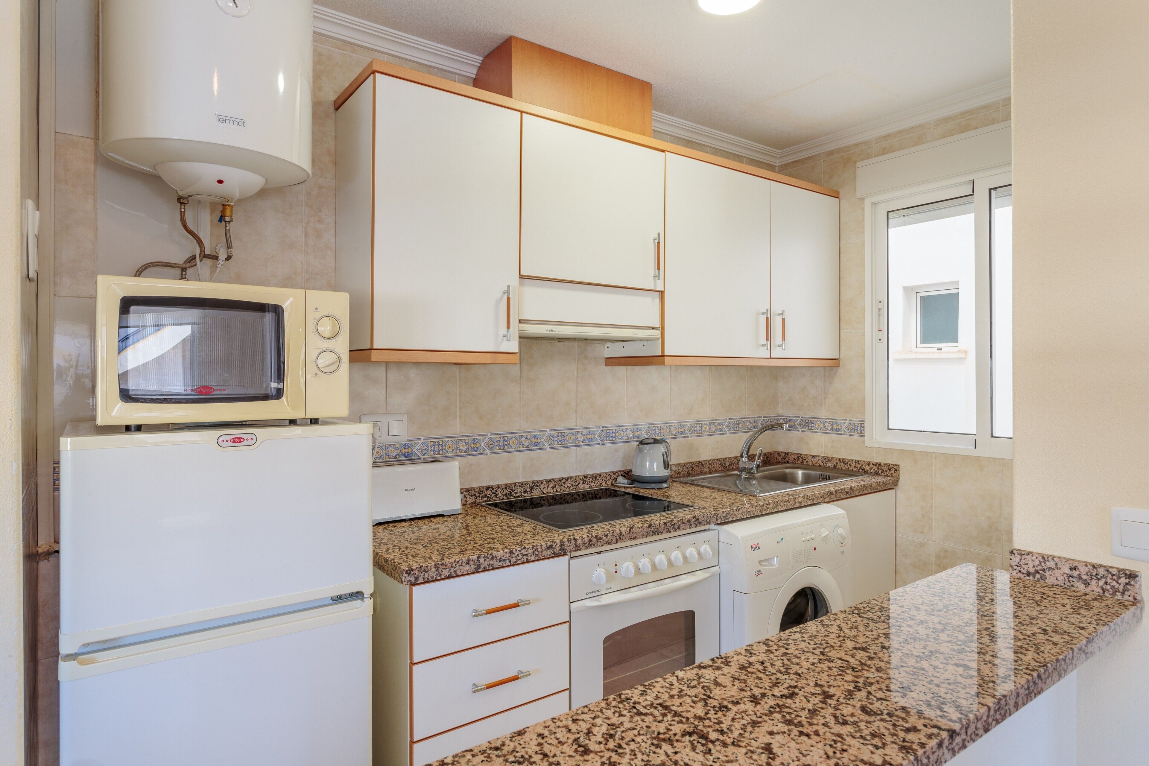 A kitchen with a microwave, oven, sink, and washing machine.