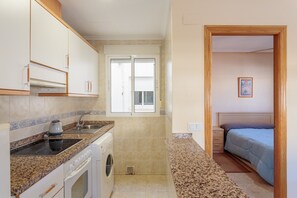 A compact kitchen with a washing machine, a built-in oven, and a window with blinds. - Apartment 'Apartamento Salamanca 4' with Shared Pool, Wi-Fi and Air Conditioning (Santa Pola)