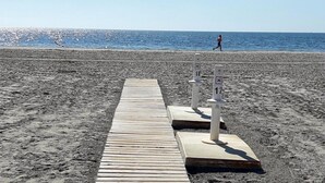 Ein Holzweg führt zu einem Strand, der von zwei weißen, mit Zahlen versehenen Säulen markiert ist.