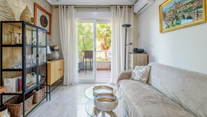 Ein Wohnzimmer mit einer Couch, einem Glastisch, einer Vitrine mit Dekoration und Blick durch eine Glastür auf einen Außenbereich.
